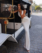 Woman in a white outfit standing next to an old-fashioned vehicle on a cobblestone street.